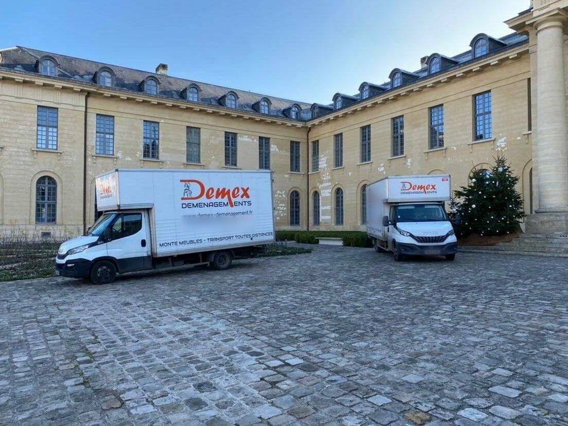 Deux camions DEMEX stationnés dans une cour pavée