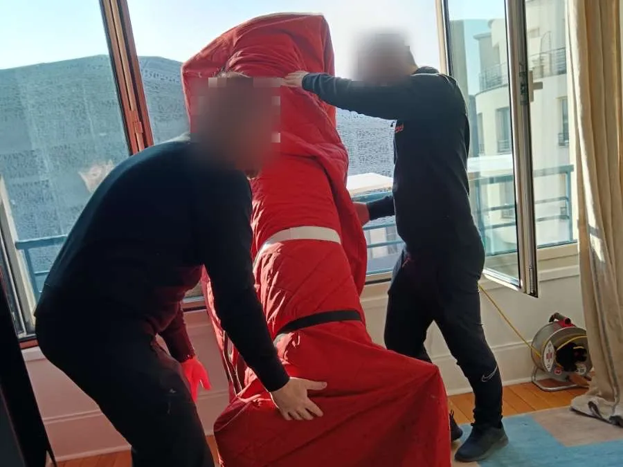 Déménageurs DEMEX manipulant un objet volumineux protégé par une housse rouge dans un appartement