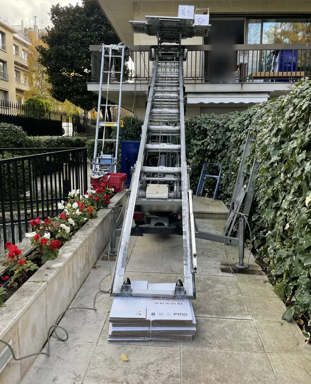 Monte-meubles DEMEX déployé jusqu’au balcon d’une résidence, cartons DEMEX au pied de l’échelle