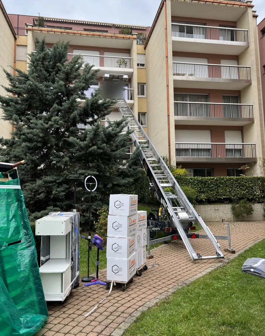 Monte-meubles déployé vers le balcon d’une résidence, cartons DEMEX empilés au pied de l’échelle